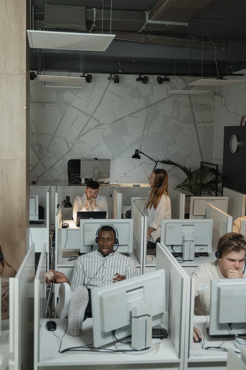 Modern office with diverse employees using computers and headsets in cubicles, providing technical support.